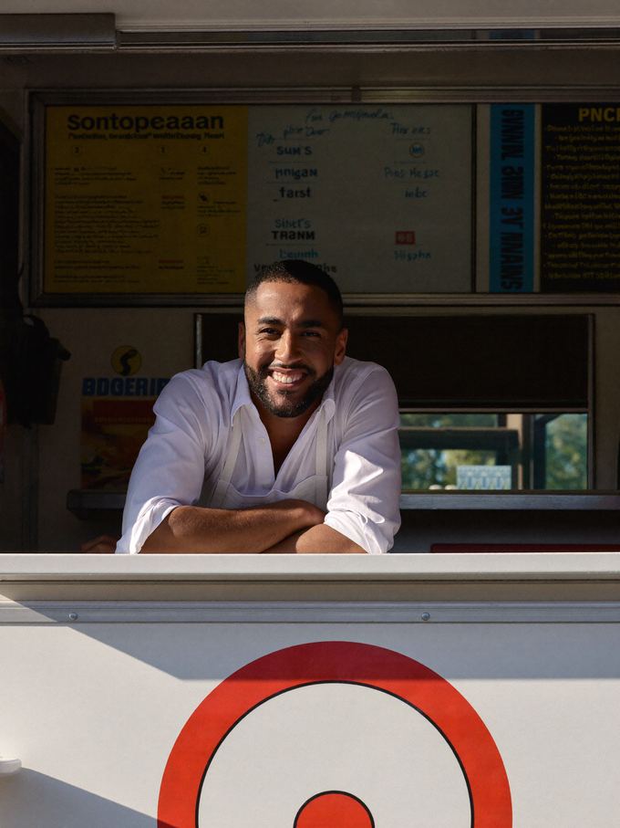 A food truck owner smiling as he leans out of his truck's service window.